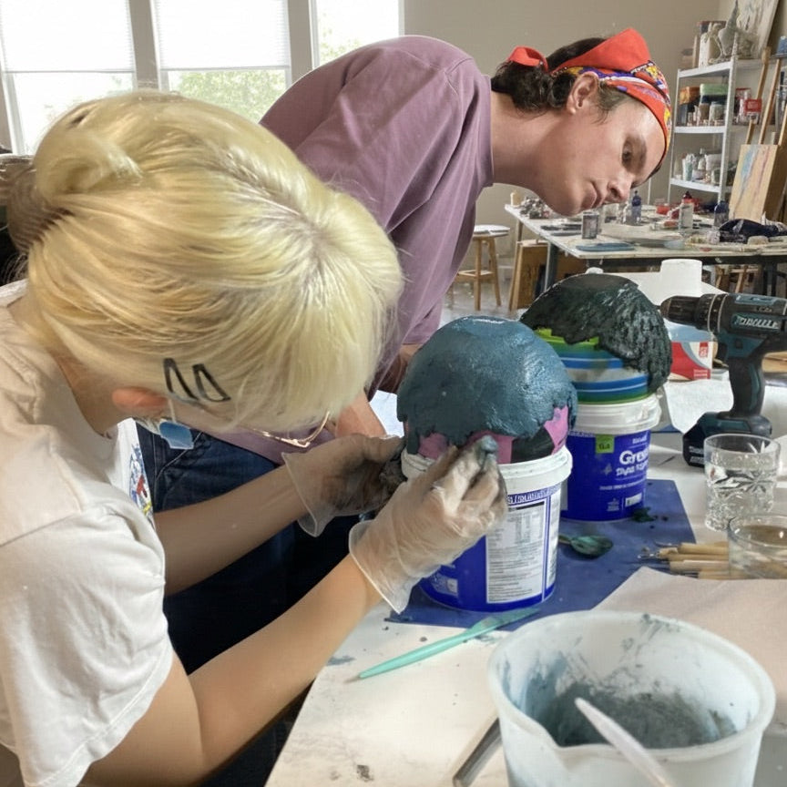 Two people working on a sculpture in a workshop setting.