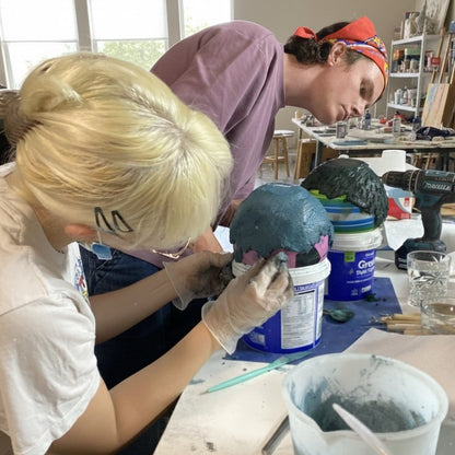 Two people working on a sculpture in a workshop setting.